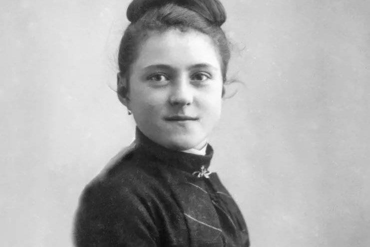 A black-and-white studio portrait of a teenage girl with her hair pinned up, wearing a high-collared dark dress, looking toward the camera.