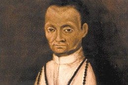 A half-length portrait of a mixed-race Dominican lay brother in a white habit and black rosary, with short dark hair and a calm, direct gaze against a dark background.