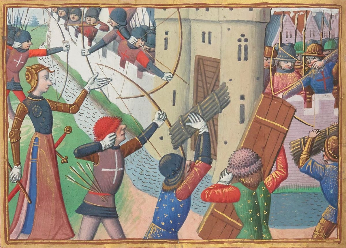 A medieval manuscript illumination showing St. Joan of Arc in white armour with a sword at her belt, standing before archers and soldiers who fire on a walled city gate defended by troops on the ramparts.