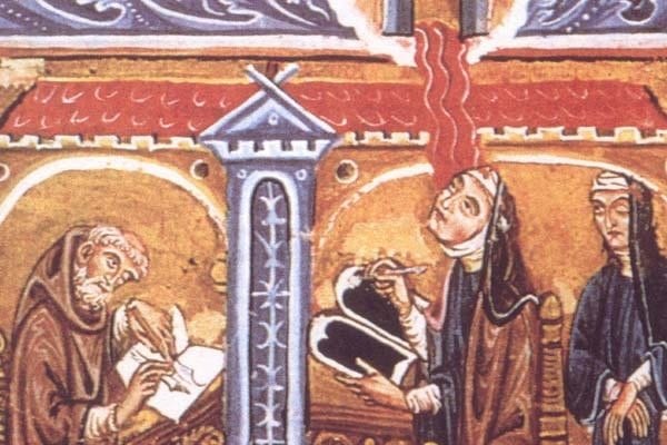 A medieval illuminated miniature showing a veiled nun, tongues of flame above her head, writing on a wax tablet; a bearded monk seated at a lectern writes in a book to her left, and a veiled nun stands watching to her right, under a red-roofed arcade.