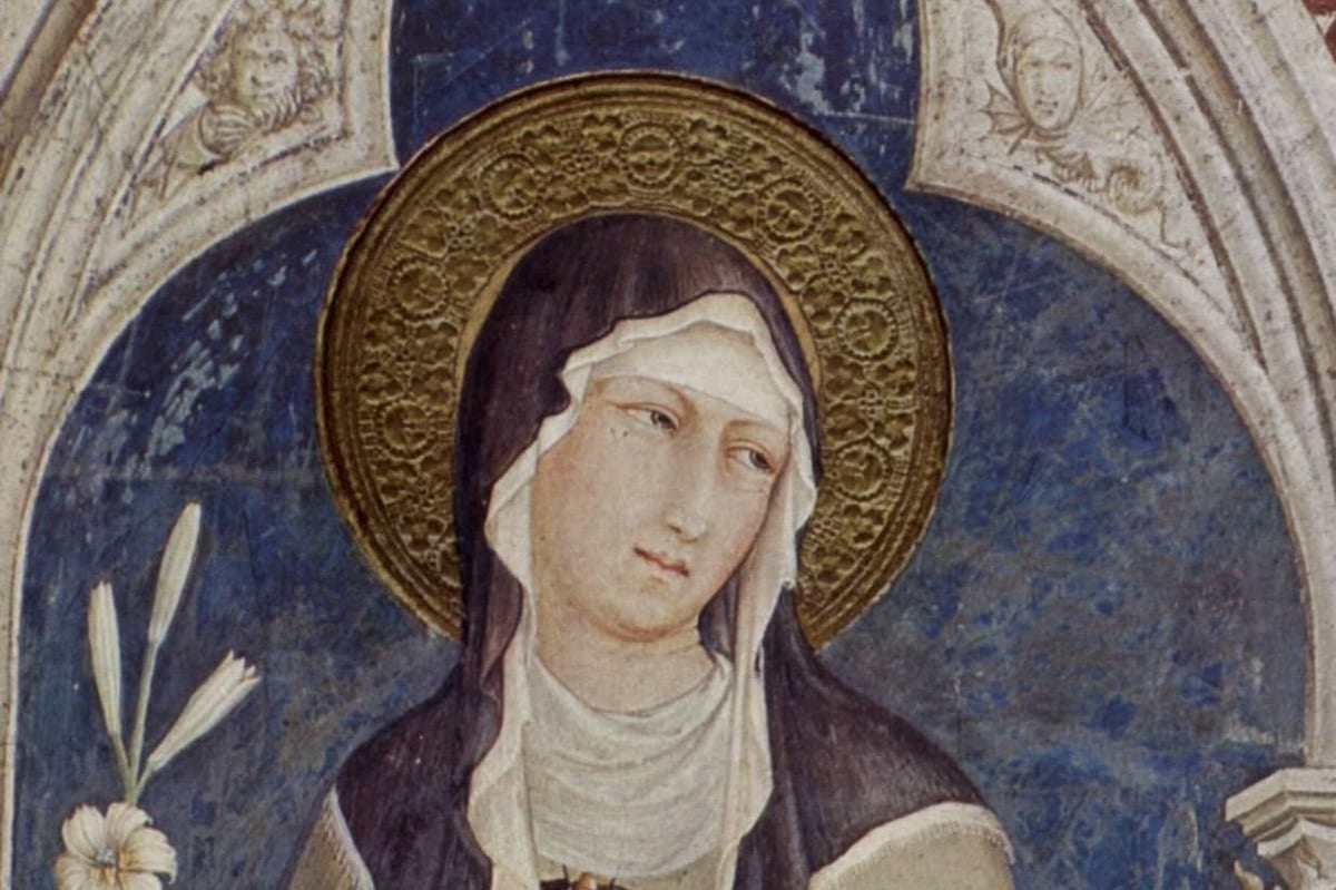 A head-and-shoulders detail of a fresco showing St. Clare of Assisi in a pale habit and dark veil, with a gold halo, standing beneath a painted Gothic arch.