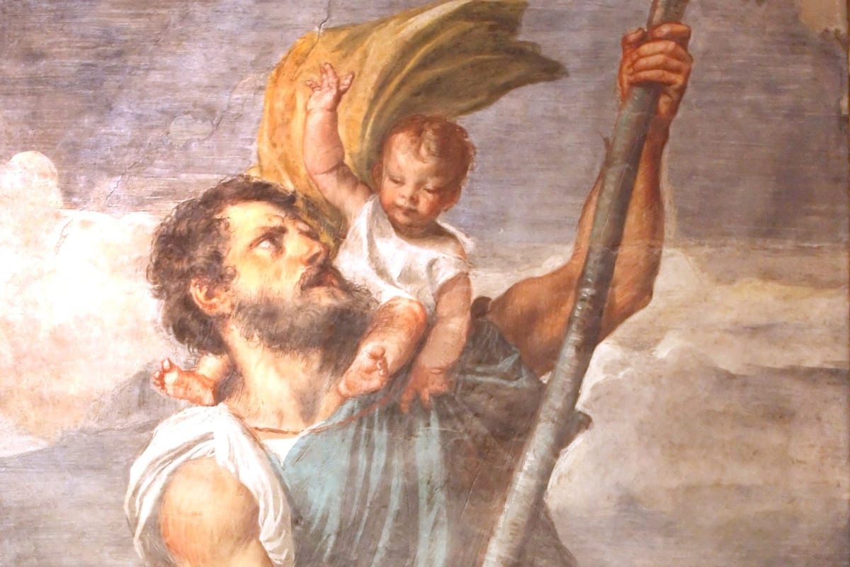 A bearded, muscular man wades through water bearing a small child on his shoulders, gripping a tall wooden staff, the child reaching up with one hand as the man looks up toward him.