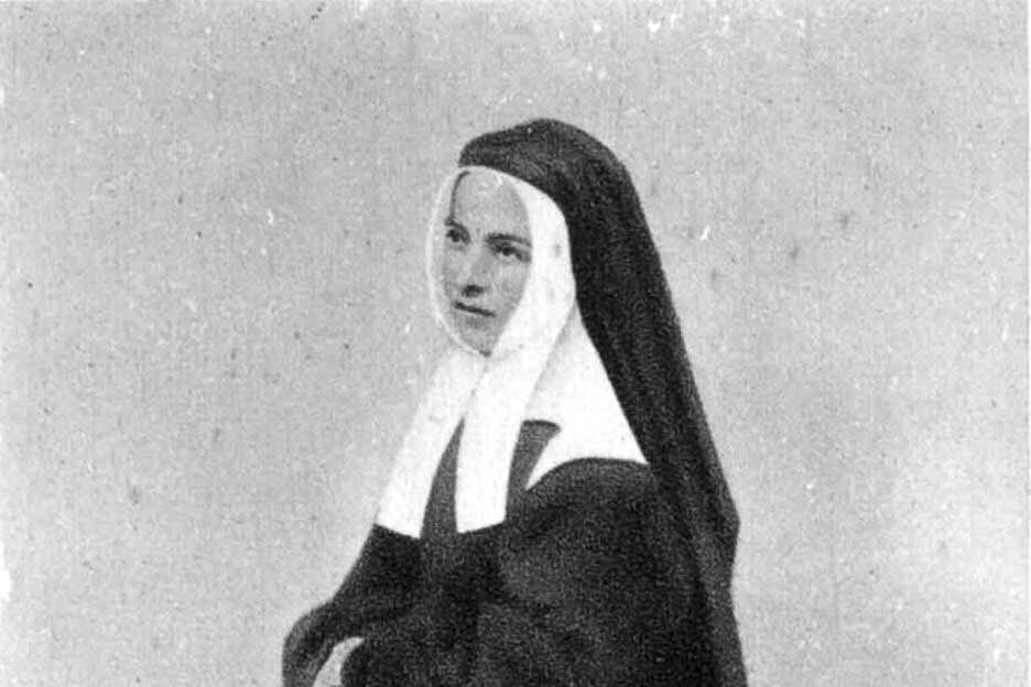 Black-and-white photograph of a young nun in a dark habit with a white coif and collar and a long black veil, her face turned slightly to one side.