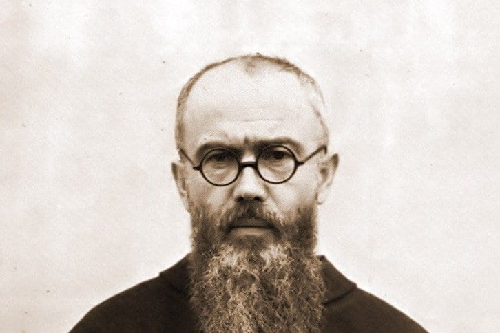 A sepia-toned portrait photograph of a bearded, balding man in round wire-rimmed glasses and a dark friar's habit, looking directly at the camera.