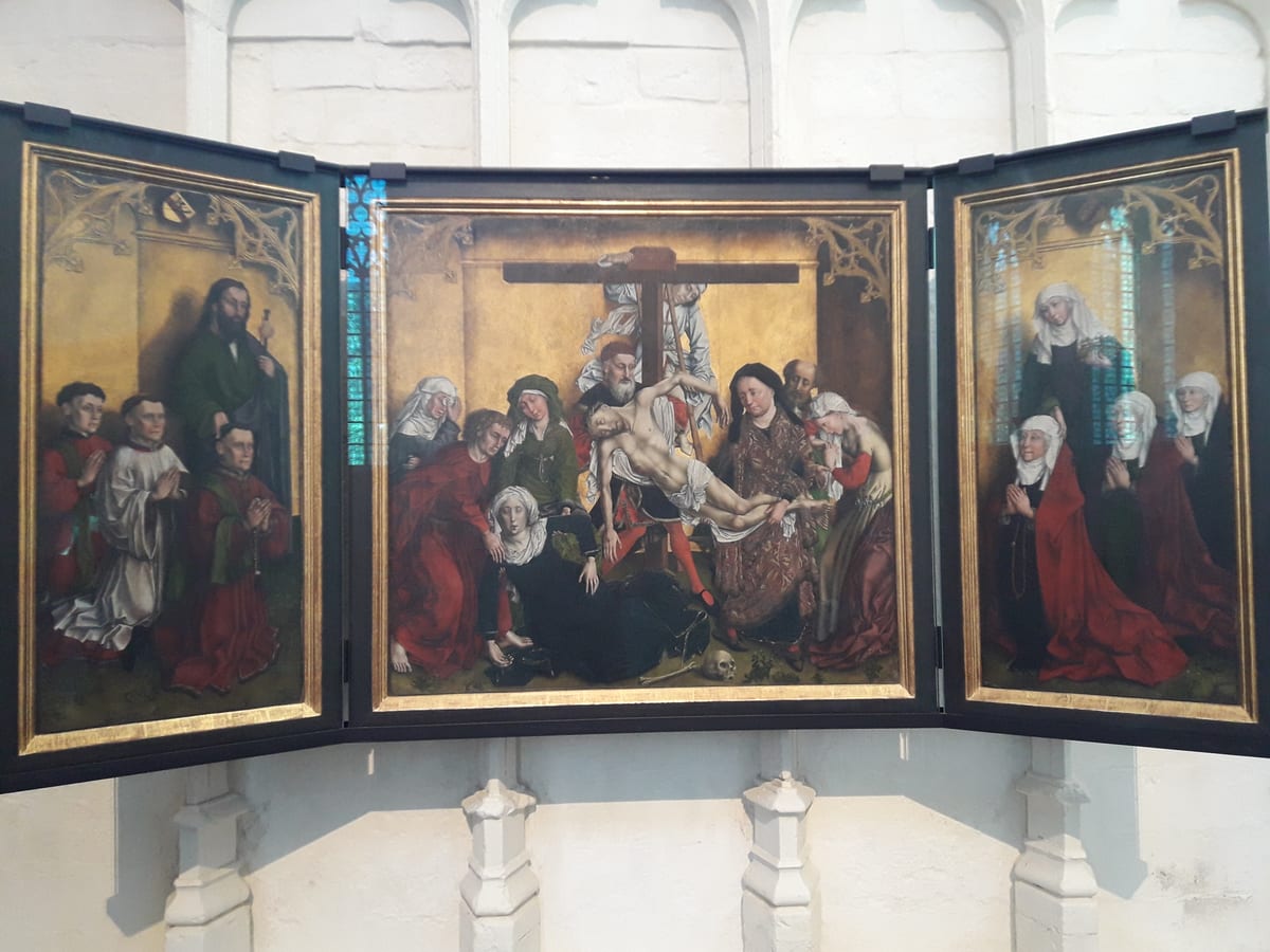 A veiled Cistercian nun in a white habit stands behind kneeling women in red robes on the right wing of a fifteenth-century Flemish triptych.