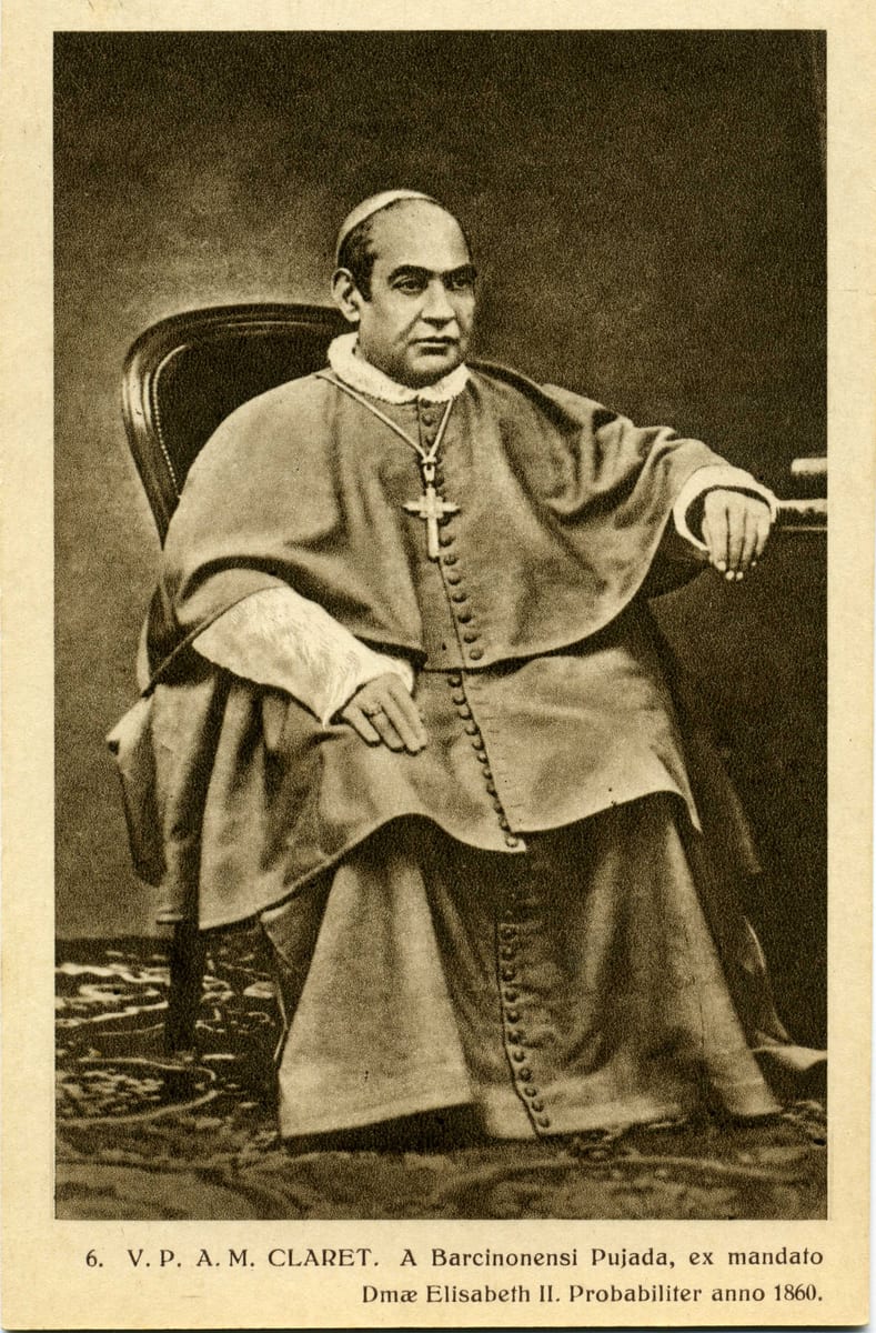 A photograph of the archbishop seated three-quarter length in a dark armchair, his right forearm resting on a draped table.