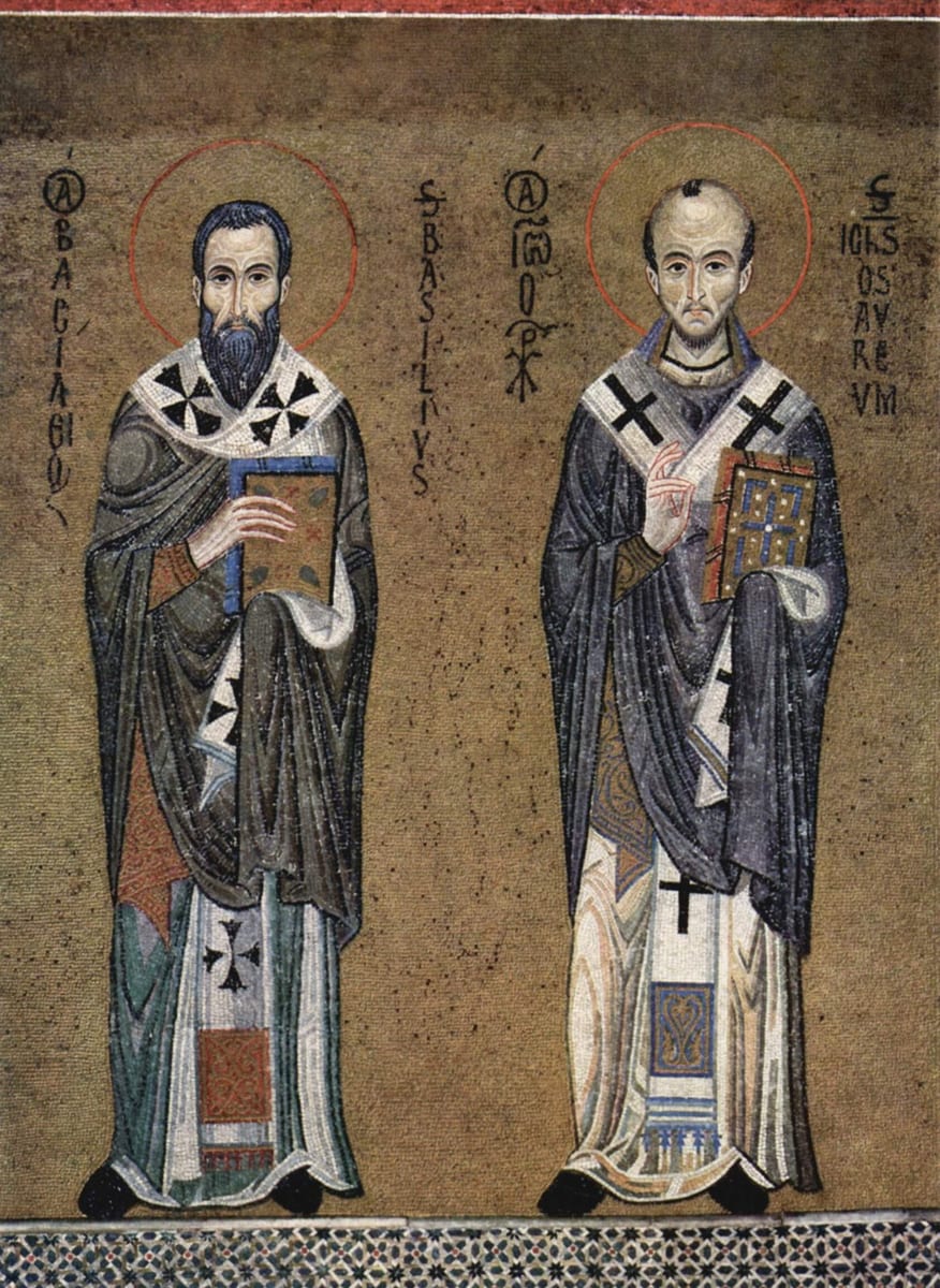 A Byzantine mosaic of St. Basil the Great and St. John Chrysostom standing side by side in bishops' vestments, each haloed and holding a jeweled Gospel book, with their names inscribed in Greek and Latin beside them.