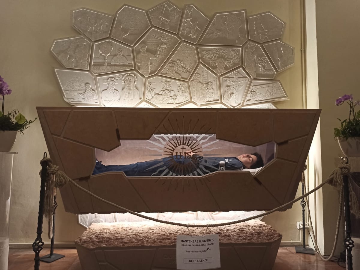 The glass-fronted tomb of St. Carlo Acutis in the Sanctuary of the Spoliation, Assisi, with his body dressed in everyday clothes.