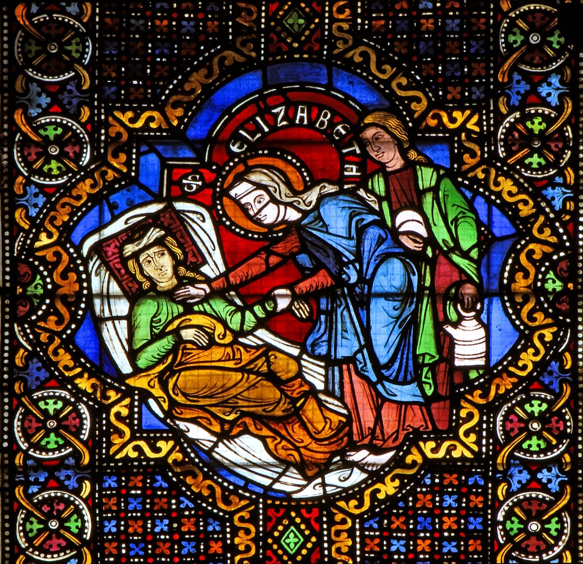 A stained-glass medallion of about 1240–1250 AD shows St. Elizabeth, veiled and haloed, bending over a sick young man in bed and holding his hand.