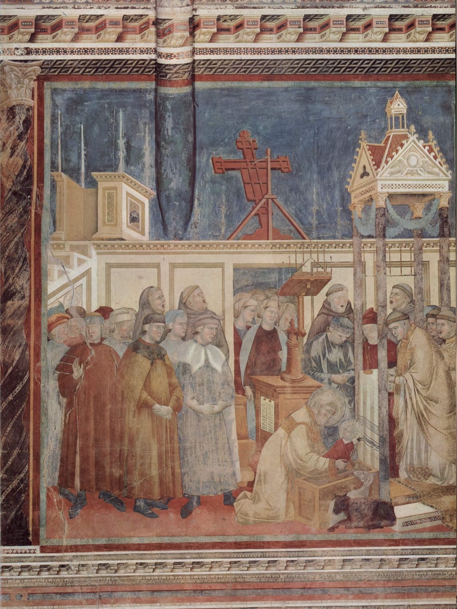 St. Francis kneels in a friar's habit in the sanctuary at Greccio holding a child above the manger, with the ox and the ass behind him, clergy singing at a lectern and the townspeople pressed at the screen.