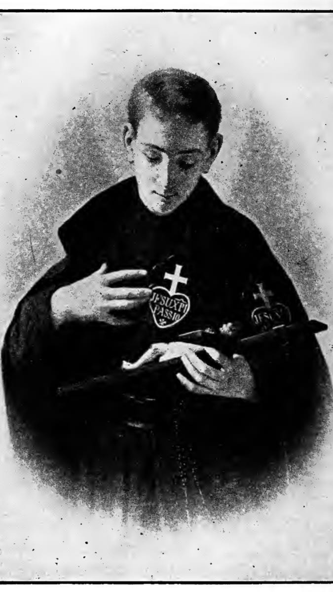 A young man in a Passionist habit holds a small heart-shaped badge marked with a cross and the words 'JESU XPI PASSIO' in one hand and a crucifix on a rosary in the other, his eyes lowered toward them.