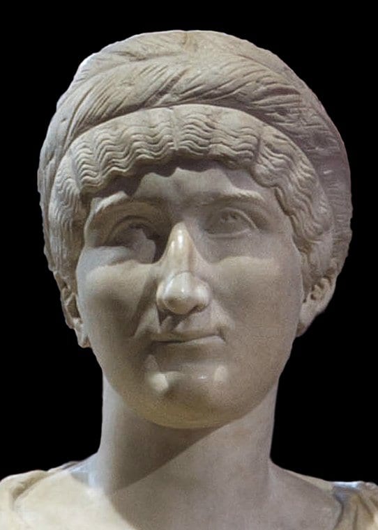 A marble portrait bust of a Roman woman with wavy hair bound in a plaited headband, her head turned slightly, gazing outward with a calm, composed expression.