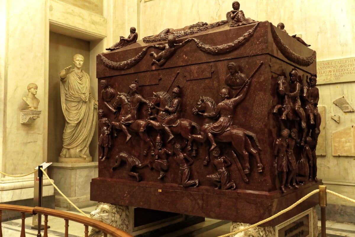 A monumental red porphyry sarcophagus carved with Roman soldiers on horseback and bound barbarian prisoners, raised on four carved lions.