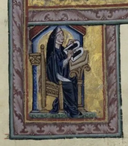 A medieval illuminated manuscript miniature showing a veiled nun with a halo seated in a carved wooden chair, holding open a book on a stand before her, set within a gilded architectural niche and framed by an ornate floral border.