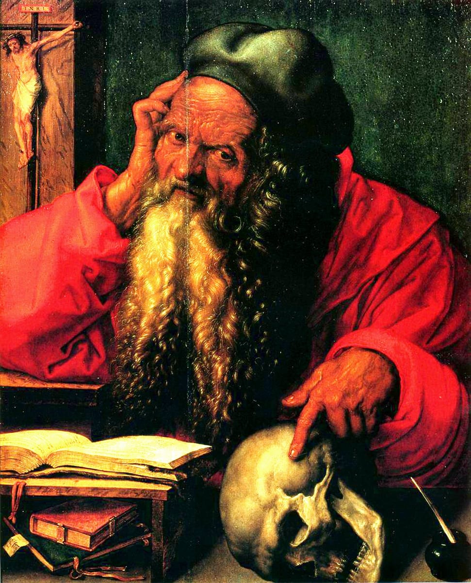An elderly, bald, long-bearded Saint Jerome in a red robe and green cap touches his temple with one hand while resting the other on a skull beside an open book, with a crucifix on the wall behind him.