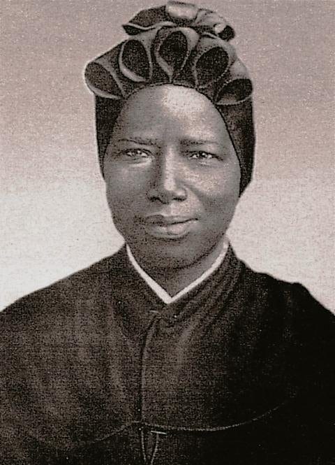 A formal black-and-white portrait of a Black African nun in religious habit and headdress, looking calmly toward the camera with a faint smile.