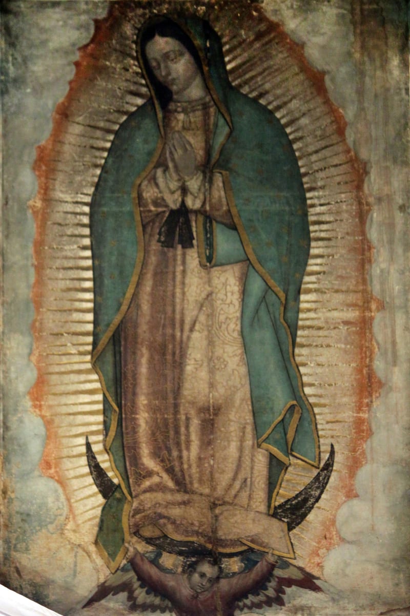 A photograph of the ayate as it hangs in the Basilica, showing the standing figure of Our Lady of Guadalupe on a coarse two-strip weave.