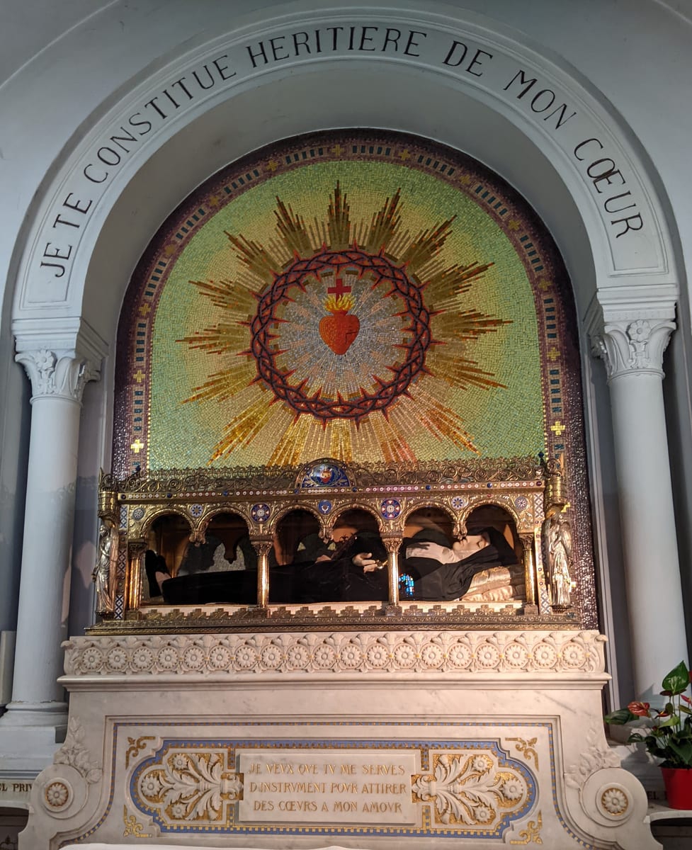 A recumbent effigy of the saint in the black Visitation habit lies behind glass beneath a gilt canopy in the chapel at Paray-le-Monial.