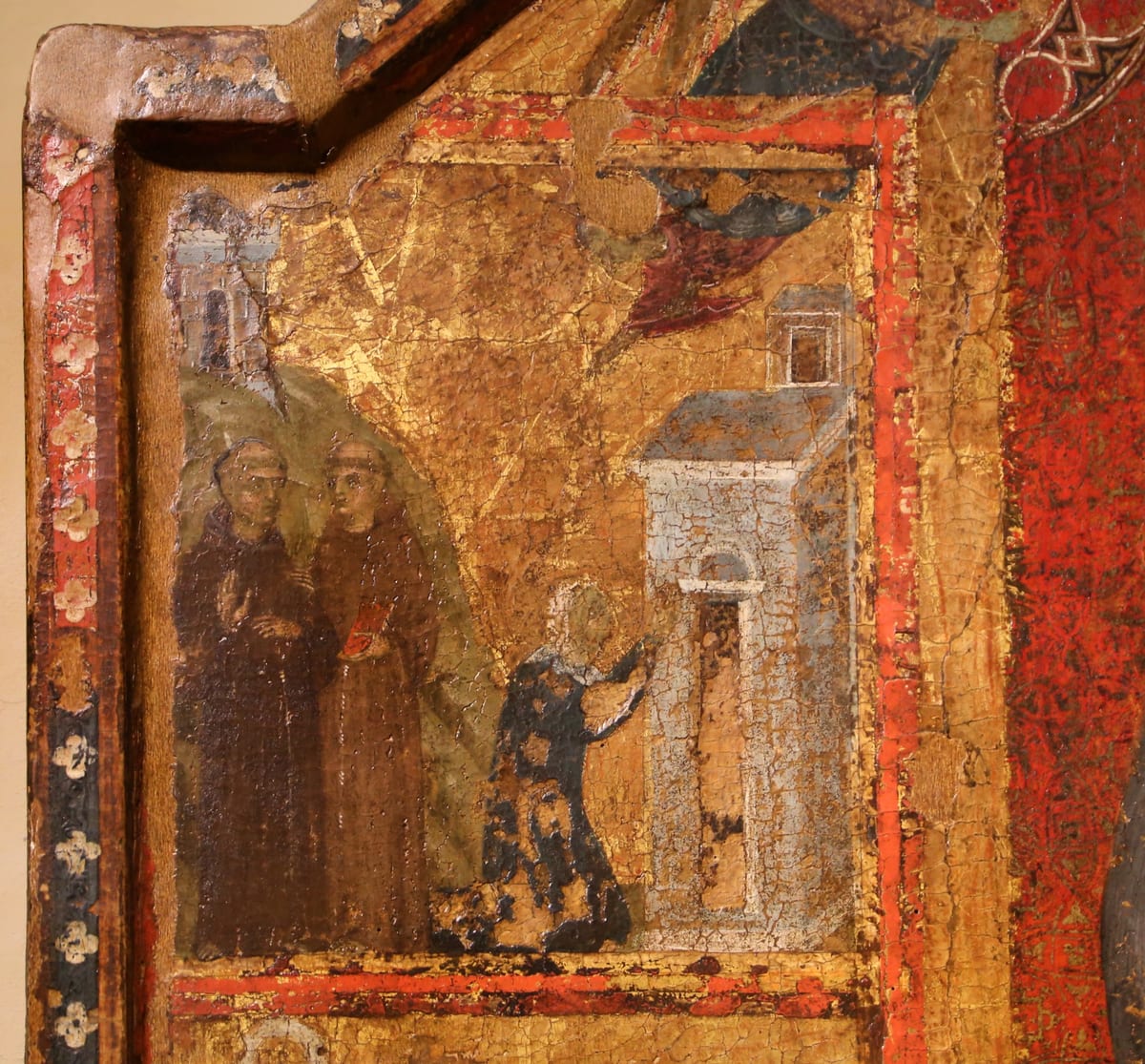 In a worn medieval panel painting, St. Margaret kneels in a dark blue patterned gown and pale veil before a small white building, while two Friars Minor in brown habits stand at the left.