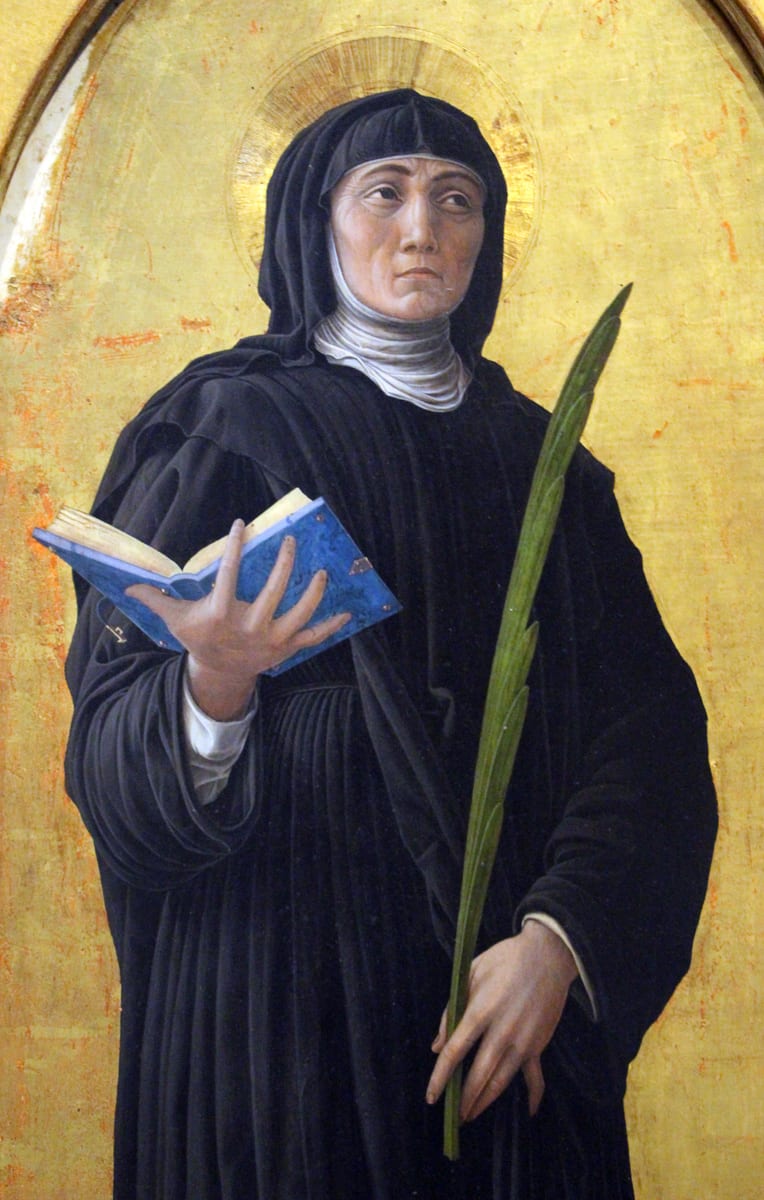 Saint Scholastica stands in the black Benedictine habit and veil, holding an open book in her right hand and a palm in her left.