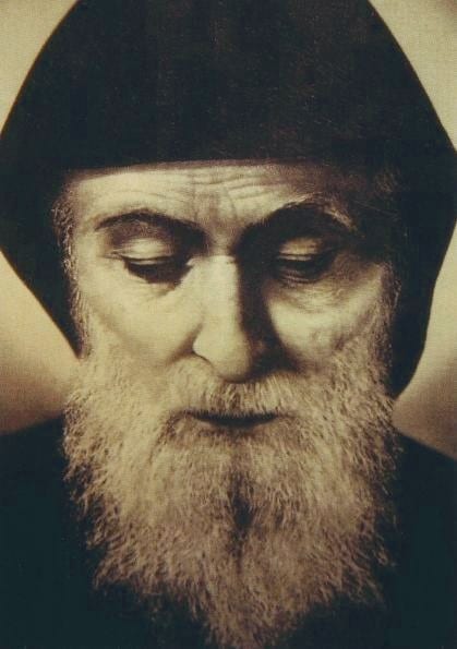 A sepia head-and-shoulders portrait of an old hooded monk with a long white beard, a deeply lined forehead and lowered eyes.
