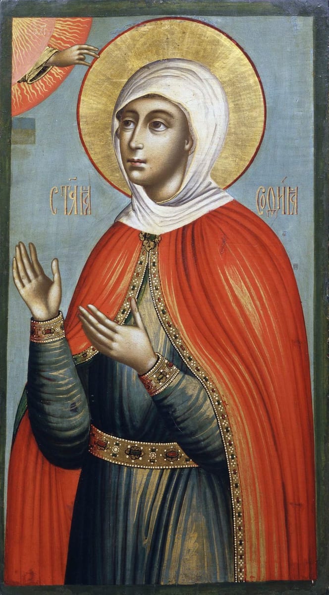 A Russian icon of a woman in a white head covering and red cloak over a dark robe, haloed in gold, hands raised in prayer, with the hand of God blessing her from a cloud at the upper left.