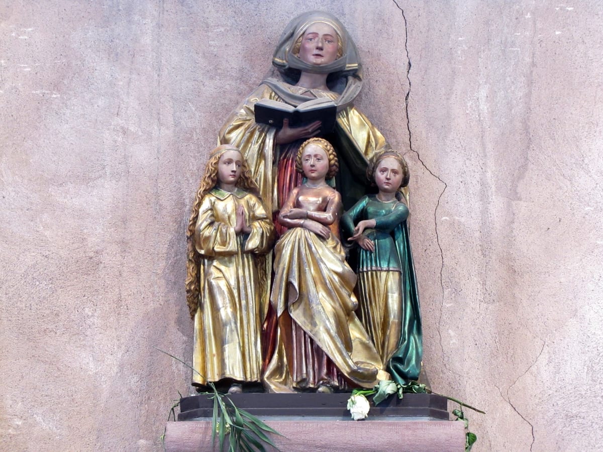 A painted and gilded wooden carving shows St. Sophia, veiled and in a gold mantle, holding an open book above her three daughters, who stand before her in gold, rose and green gowns.