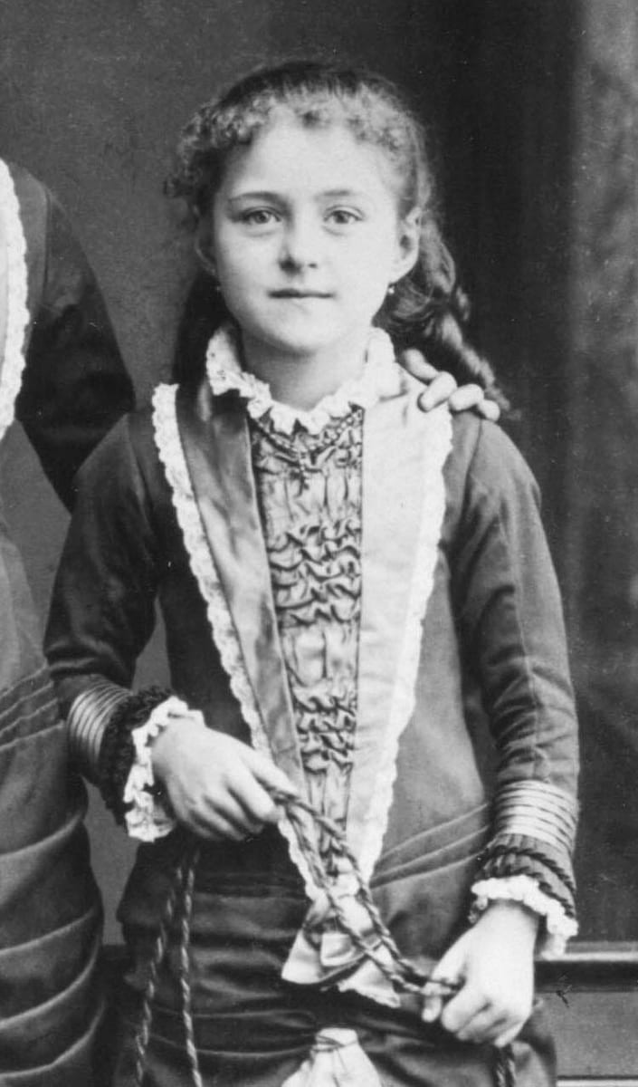 St. Thérèse at eight years old, standing upright in a dark buttoned frock in a Lisieux photographer's studio in 1881 AD.