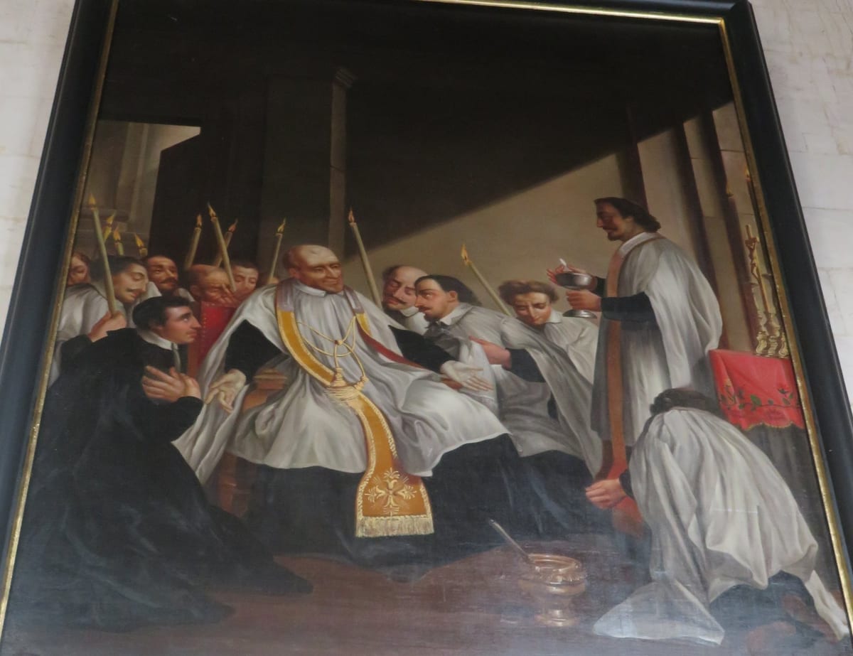 Saint Vincent de Paul sits in a chair in a bare room receiving the last sacraments, his priests and brothers around him.